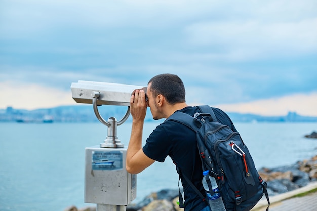 Un turista con uno zaino sulla schiena guarda attraverso il binocolo turistico sul ponte di osservazione