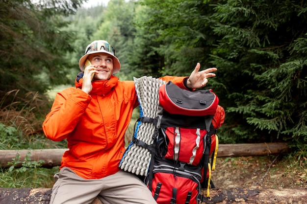 un turista maschio con uno zaino e attrezzature da escursione si siede nella foresta e parla al telefono