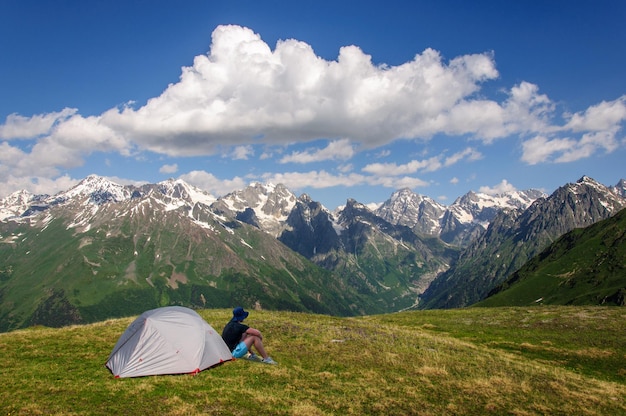 Un turista siede vicino alla sua tenda grigia sulle montagne del Caucaso in Georgia