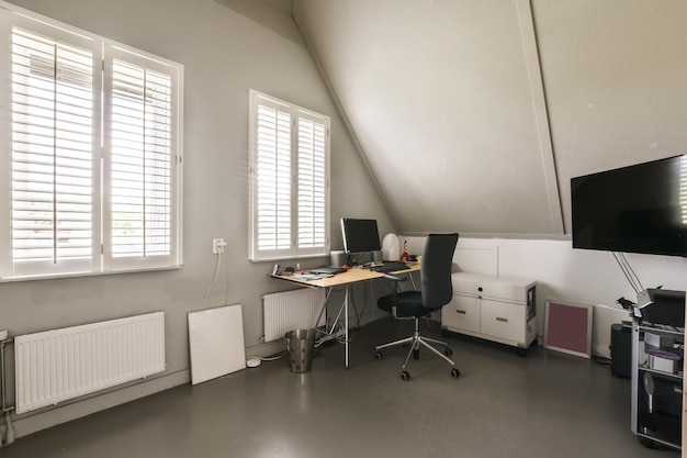 un ufficio a casa con persiane bianche sulle finestre e una scrivania per computer di fronte a una grande finestra