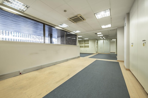 Un ufficio vuoto con pavimenti in moquette bicolore, uno spazio con pareti divisorie e schedari ovunque, soffitti tecnici e aria condizionata