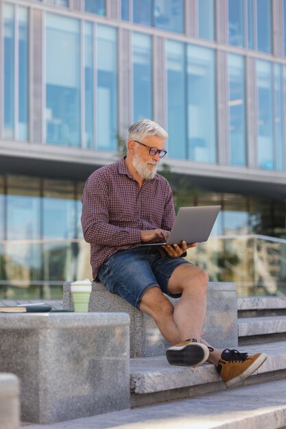 Un uomo adulto dai capelli grigi con la barba è seduto in ufficio e lavora su un laptop