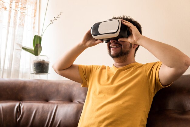 Un uomo adulto medio latino indossa un visore VR ed è seduto sul divano