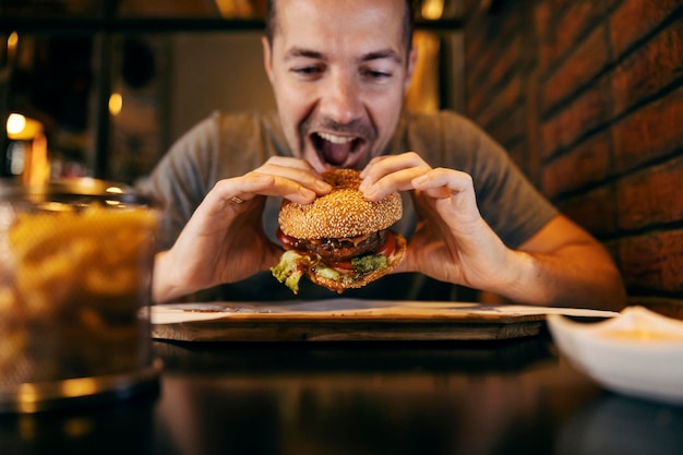 Un uomo affamato che morde un delizioso hamburger in un fast food