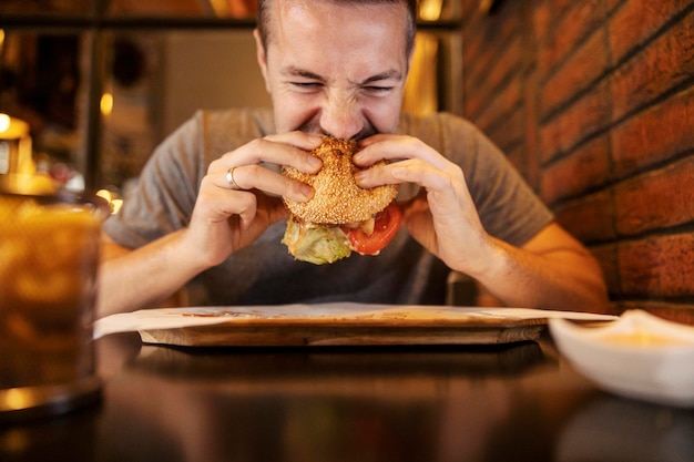 Un uomo affamato seduto in un ristorante e che mangia un delizioso hamburger.