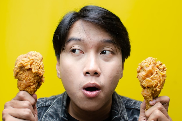 Un uomo affamato tiene un pollo fritto isolato sullo sfondo giallo.