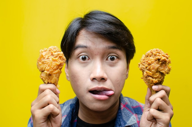 Un uomo affamato tiene un pollo fritto isolato sullo sfondo giallo.