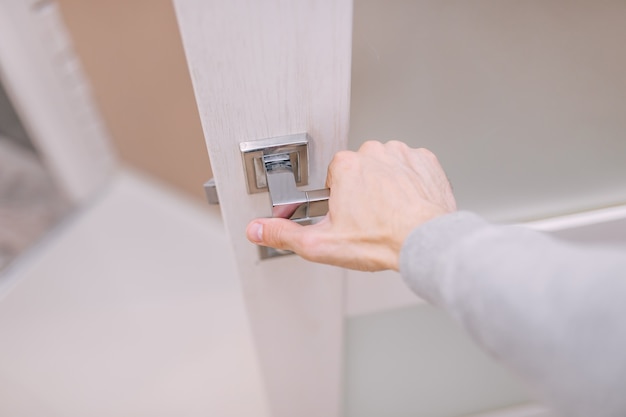 Un uomo afferra la maniglia con la mano e apre la porta per entrare nella stanza.