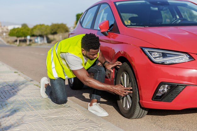 Un uomo afroamericano controlla la gomma di un'auto rossa con un giubbotto giallo