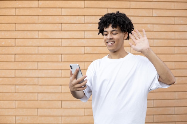 Un uomo afroamericano felice che tiene un telefono e saluta la fotocamera durante lo studio online