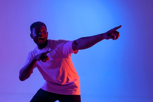 un uomo afroamericano sorpreso che punta con la mano in avanti nell'illuminazione al neon pubblicizzata dal ragazzo
