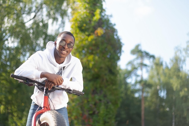 Un uomo afroamericano sorridente con una bicicletta in un parco pubblico Sport e ricreazione