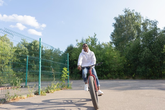 Un uomo afroamericano sorridente va in bicicletta attraverso un parco pubblico Sport e ricreazione