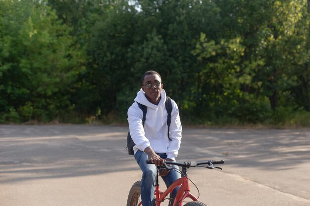 Un uomo afroamericano sorridente va in bicicletta attraverso un parco pubblico Sport e ricreazione