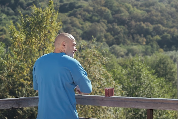 un uomo al mattino su un balcone aperto beve un caffè e ammira la natura delle montagne