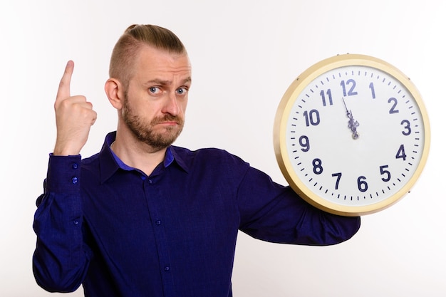 Un uomo alla moda tiene un grande orologio da parete e punta il dito su bianco