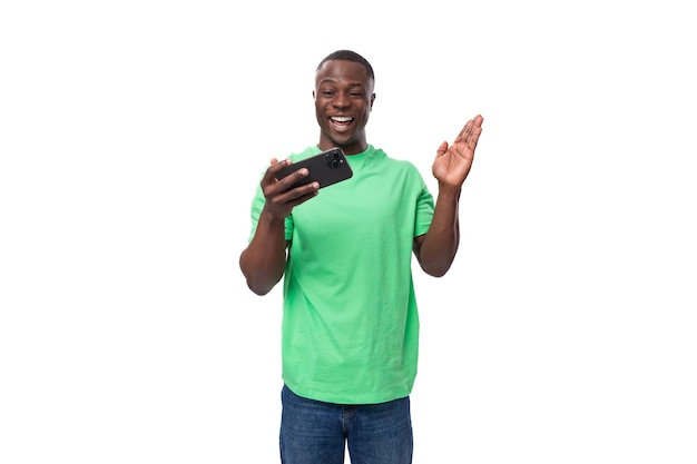 Un uomo americano di un anno vestito con una maglietta basic verde chiaro sta guardando un video su uno smartphone