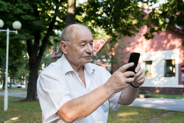 Un uomo anziano cammina da solo nel parco in estate un moderno uomo d'affari pensionato in una camicia bianca