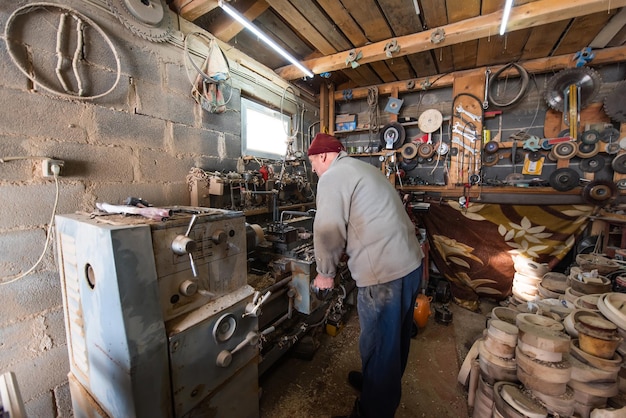 Un uomo anziano che elabora il legno su un tornio e fa piatti di legno nel laboratorio