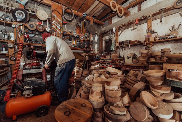 Un uomo anziano che elabora piatti di legno in officina nel modo tradizionale manuale