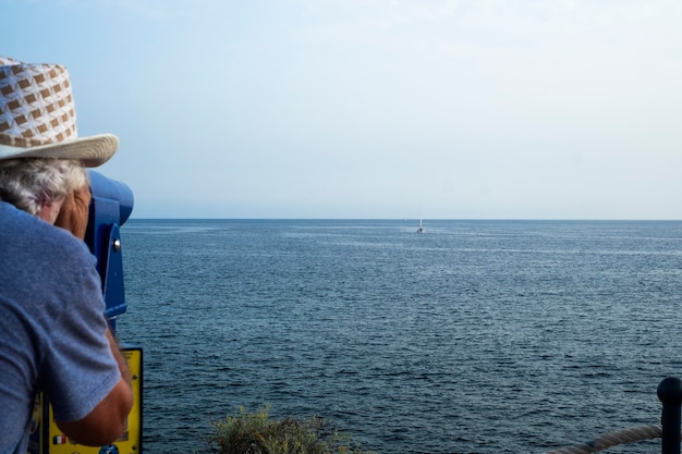 Un uomo anziano che guarda attraverso il telescopio turistico verso l'orizzonte