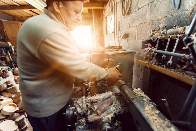 Un uomo anziano che lavora il legno su un tornio e fa piatti di legno in officina