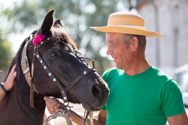 Un uomo anziano con un cappello di paglia sorride a un cavallo