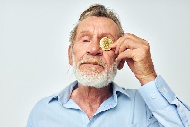 Un uomo anziano con una camicia blu copre gli occhi di una moneta bitcoin