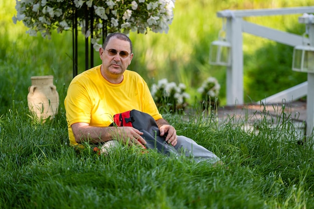 Un uomo anziano con uno zaino si siede sull'erba in un parco in una giornata di sole