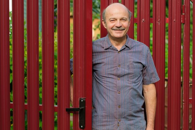 Un uomo anziano incontra gli ospiti in una recinzione di metallo rosso