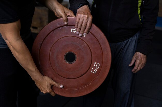 Un uomo anziano latinoamericano irriconoscibile e il suo allenatore tengono in mano un disco di peso che usano per esercizi di riabilitazione e terapia in palestra Concetto di stile di vita sano