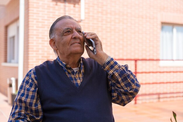 Un uomo anziano nel giardino di una casa di cura o di una casa di riposo in una soleggiata giornata estiva che guarda le tecnologie telefoniche negli anziani