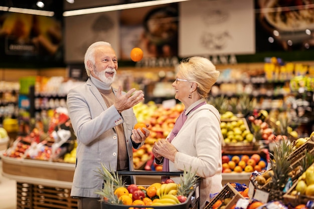 Un uomo anziano si destreggia con la frutta mentre sua moglie lo guarda