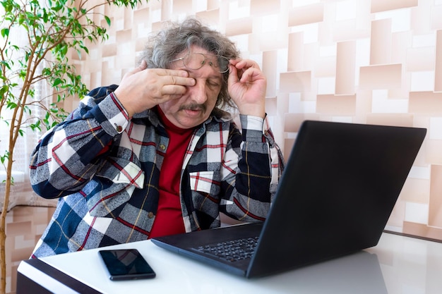 Un uomo anziano si toglie gli occhiali dopo un lungo lavoro al computer