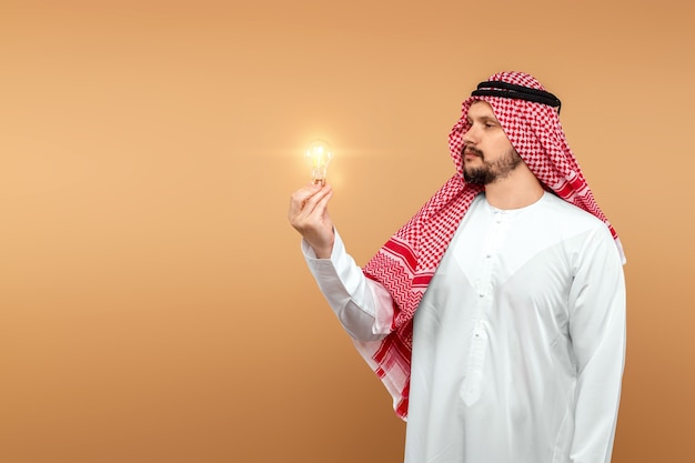 Un uomo arabo tiene un costume nazionale con una lampadina in mano. Idea di concetto, pensiero.