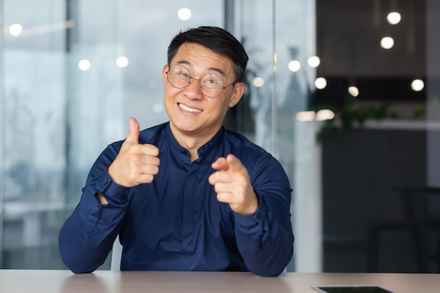 Un uomo asiatico di successo all'interno dell'ufficio sta guardando la webcam mentre parla durante una videochiamata