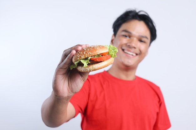 Un uomo asiatico felice che tiene in mano e mostra un delizioso hamburger alla telecamera