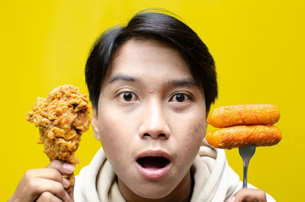 Un uomo asiatico felice e sorpreso tiene un pollo fritto e una salsiccia con un'espressione di wow isolata