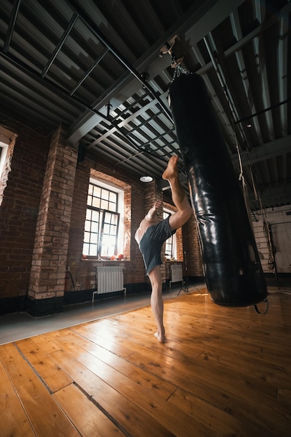 Un uomo atletico che si allena con un sacco da boxe in palestra Calciando il sacco con una gamba