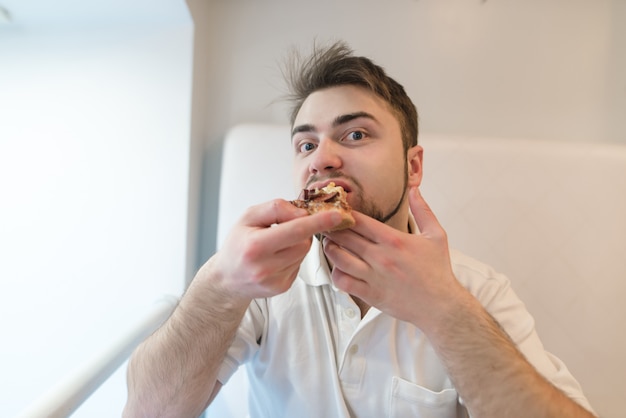 Un uomo barbuto bello mangia una pizza appetitosa e guarda la telecamera. Pizza a pranzo.