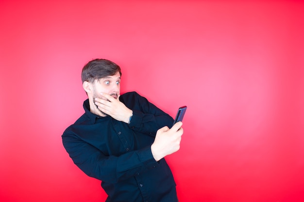 Un uomo barbuto con una camicia nera guarda stupito lo schermo del telefono