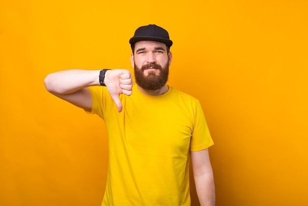 Un uomo barbuto sta mostrando il segno di antipatia vicino a un muro giallo perché è insicuro