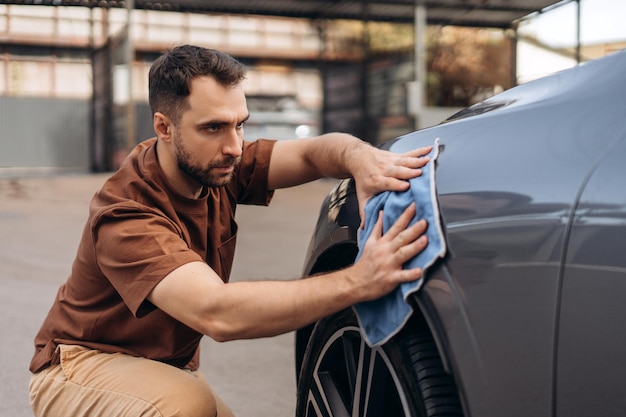 Un uomo bello e barbuto che asciuga un SUV bianco con un panno in microfibra alla stazione di self-service