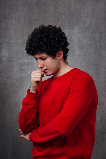 Un uomo bello e sicuro di sé con un maglione rosso guarda da un lato su uno sfondo grigio