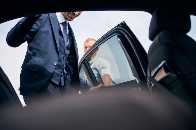 Un uomo brunetta allegro che indossa un vestito elegante che entra in un'auto per un viaggio d'affari