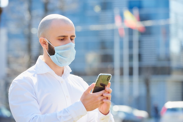 Un uomo calvo che fa affari con uno smartphone indossa una maschera medica