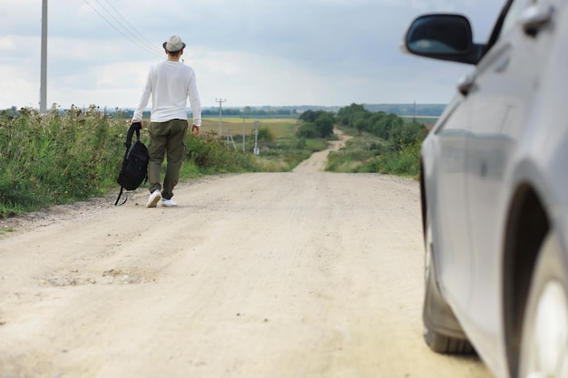 Un uomo cammina lungo una strada di campagna. Autostoppista in giro per il paese. Un uomo ferma un'auto di passaggio sulla strada.