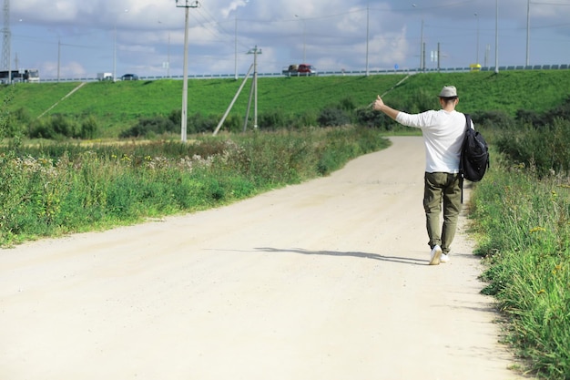 Un uomo cammina lungo una strada di campagna Autostoppista in giro per il paese Un uomo ferma un'auto di passaggio sulla strada