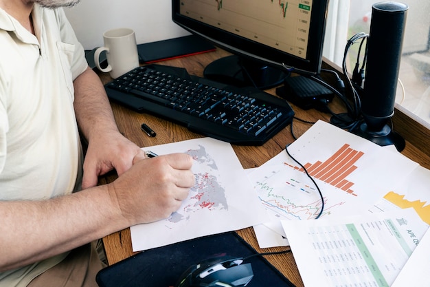 Un uomo caucasico che studia documenti con mappe, tabelle e grafici.