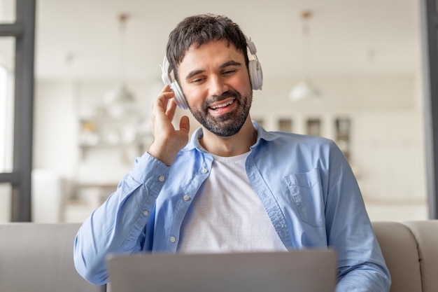 Un uomo che indossa le cuffie si siede su un divano nella sua casa sorridendo mentre ascolta la musica che sta lavorando